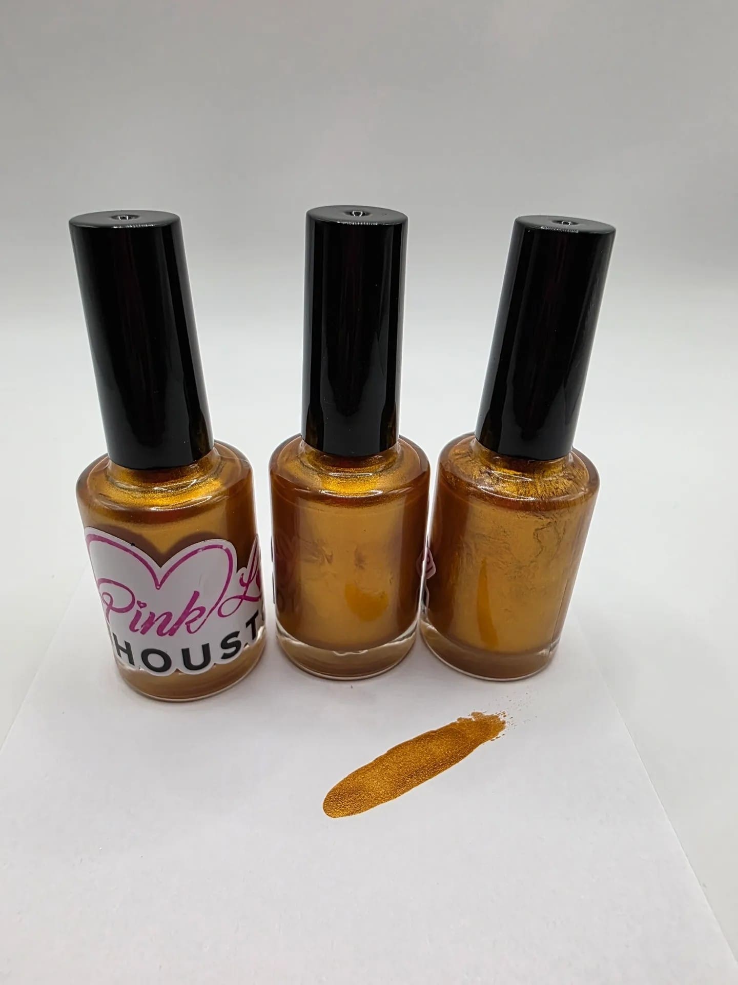 Three gold nail polish bottles with swatch.