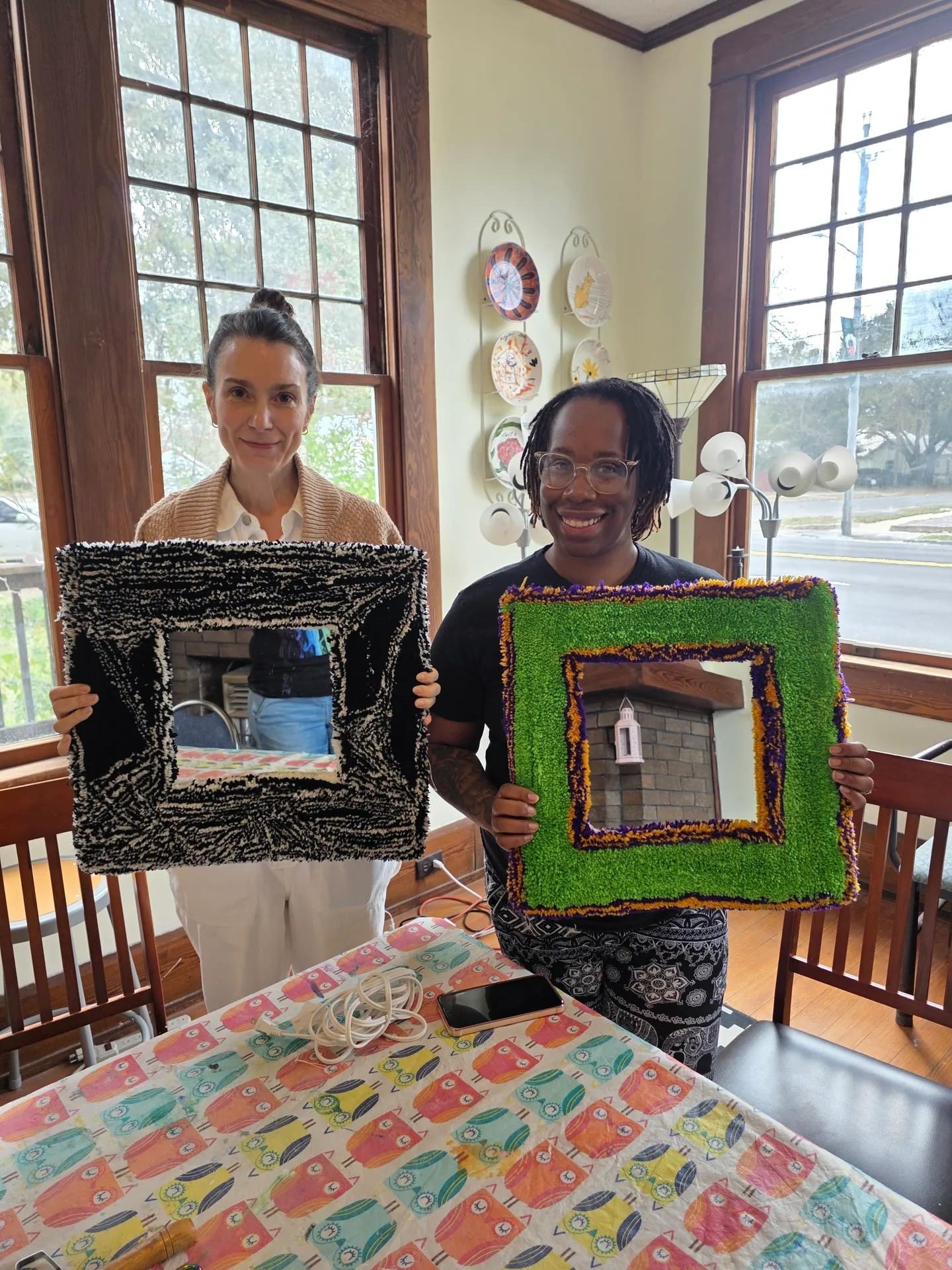 Two people holding colorful framed mirrors indoors.