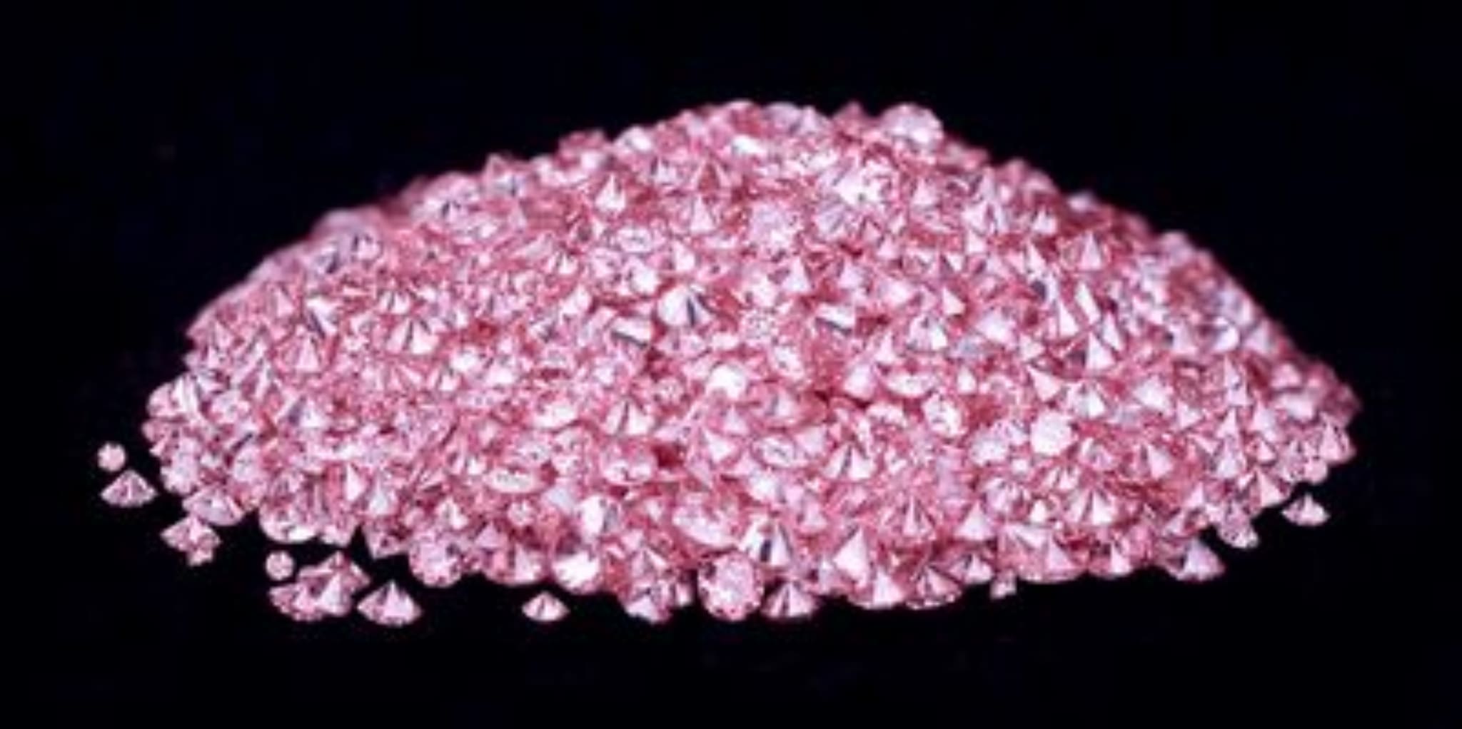 A pile of small pink gemstones against a black background.