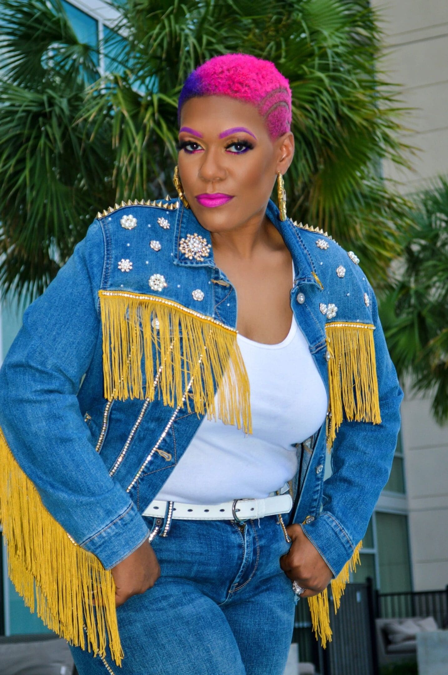 Woman in a stylish denim jacket with gold fringe and white top.