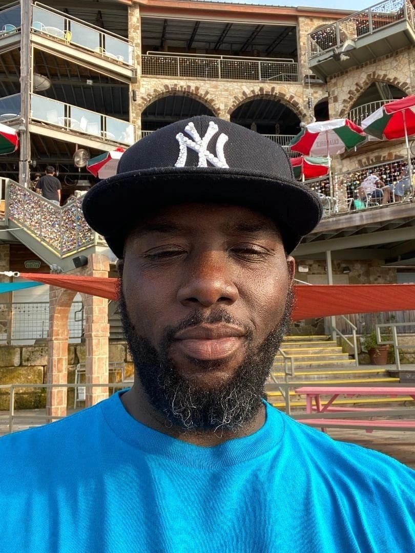 Man in a blue shirt and black Yankees cap outdoors.